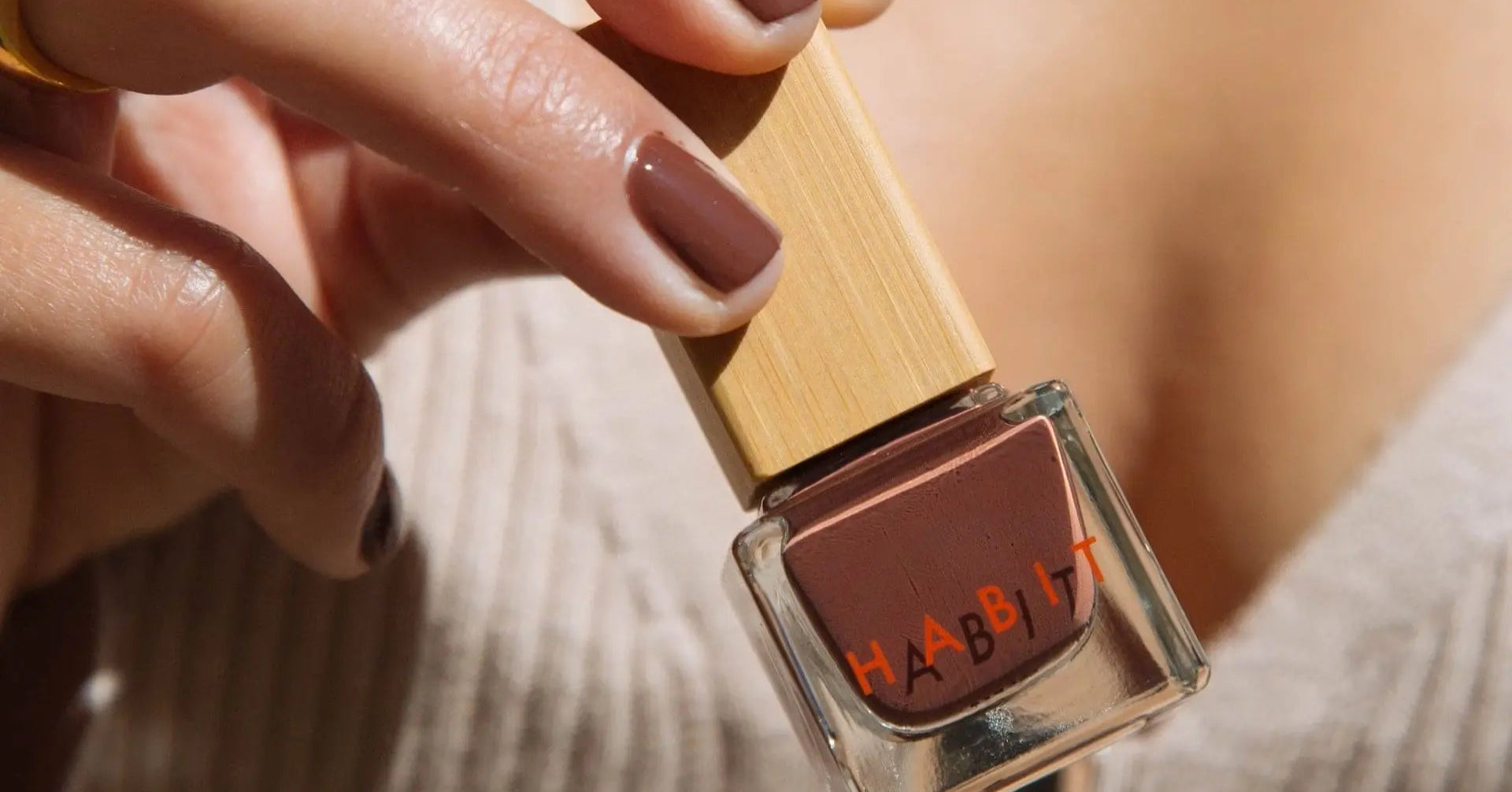 Hand holding a bottle of Habit brown nail polish with a blurred background