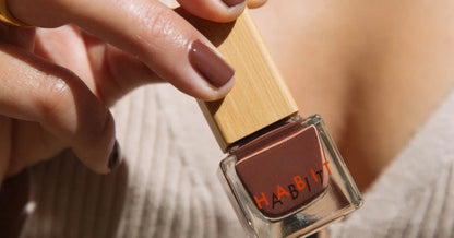 Hand holding a bottle of Habit brown nail polish with a blurred background